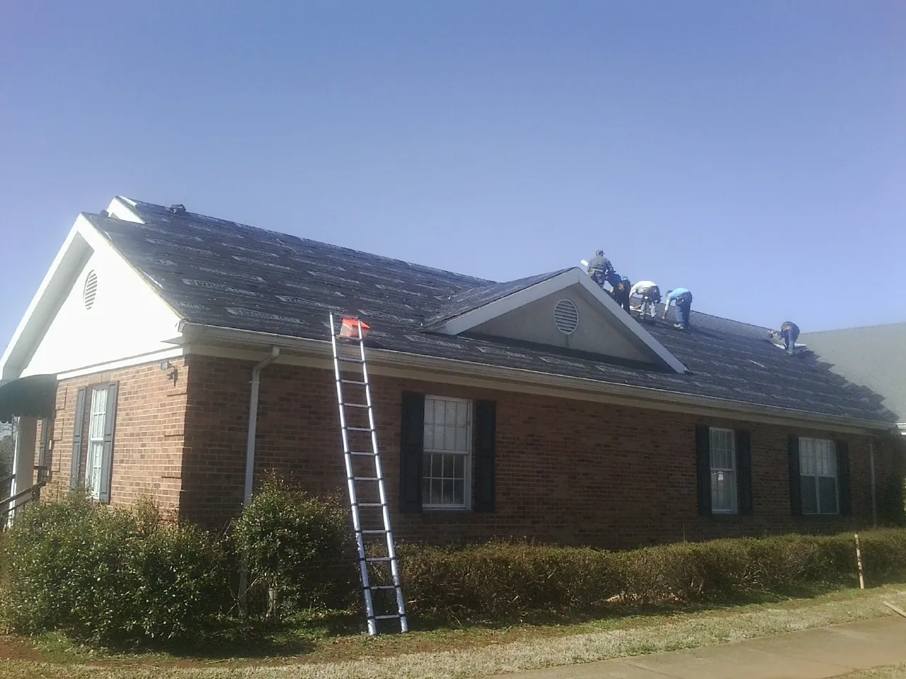 Crew tearing shingles off a brick ranch roof with a ladder set — Emergency Roof Repair work by our crew in Montreat