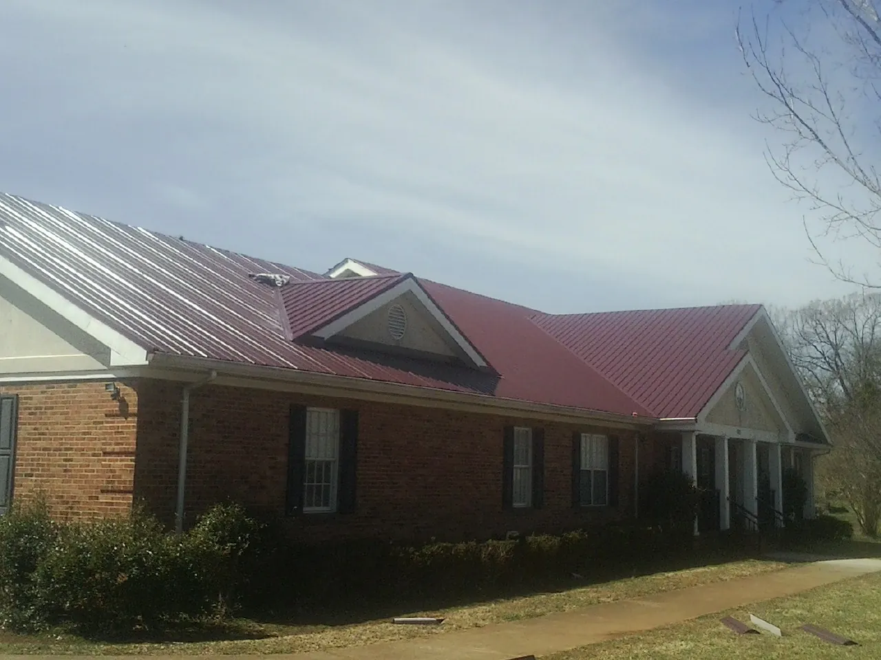 Red metal roof with gabled entries on a long brick building, from a Hail Damage Roof Repair job in Montreat