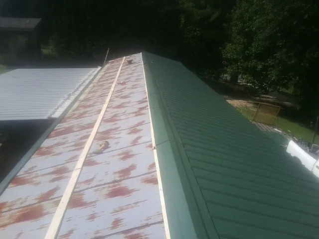 Old rusted panels beside newly installed green metal roofing — Wind Damage Roof Repair by Roofing Brothers in Montreat