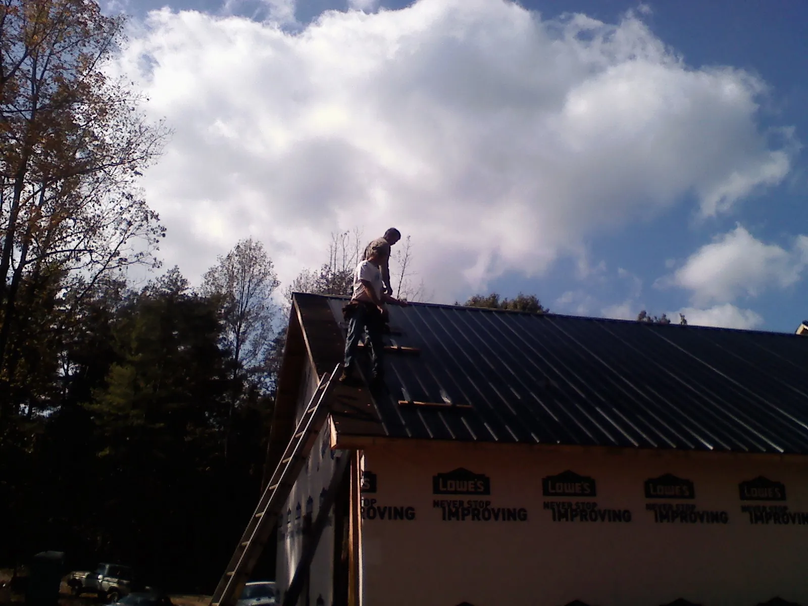 Roofer fastening dark metal panels high against a cloudy sky, from a Roof Inspection job in Montreat