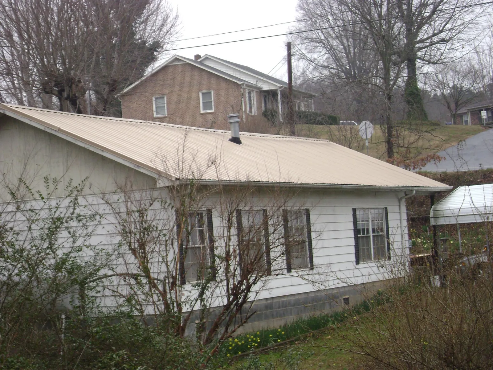 Tan metal roof on a white sided house set into a hillside — Commercial Roofing by Roofing Brothers in Montreat