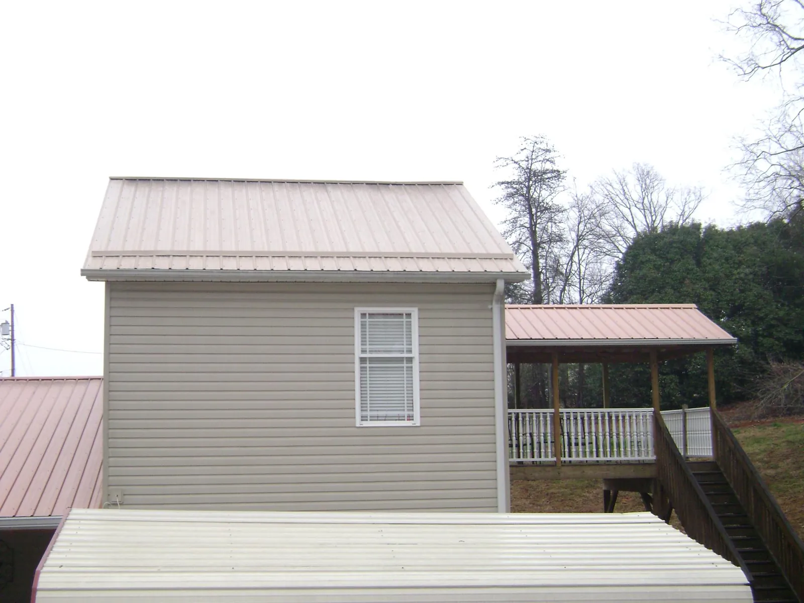 Tan metal roofs on a two story addition and attached porch, from a Roof Replacement job in Montreat